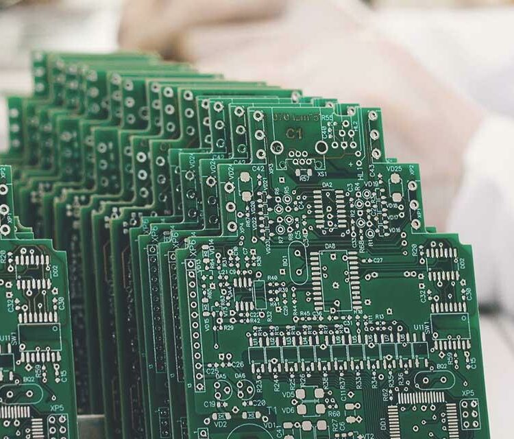 Stacks of green printed circuit boards (PCBs) lined up for testing in a manufacturing facility.