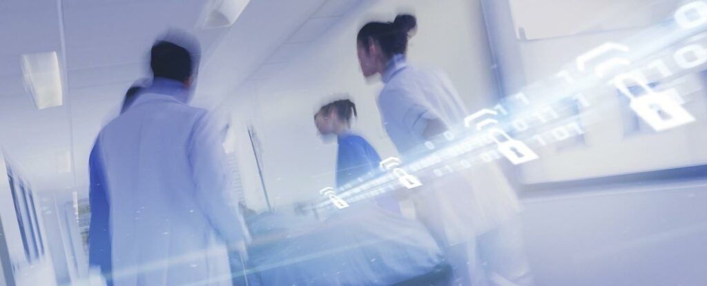 Healthcare workers moving through a hospital corridor with digital overlays of padlocks and binary code, symbolizing secure data transmission in wireless medical devices.