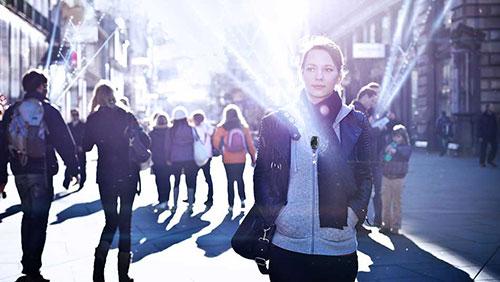 A woman walking in a busy city street with sunlight shining in the background.