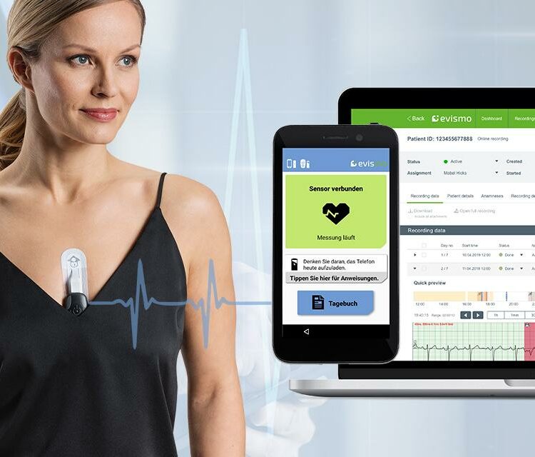 Woman wearing a wireless ECG monitoring device, with a smartphone and laptop displaying real-time heart data.